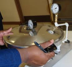 Person holding the lid of a metal pressure canner with attached gauges.