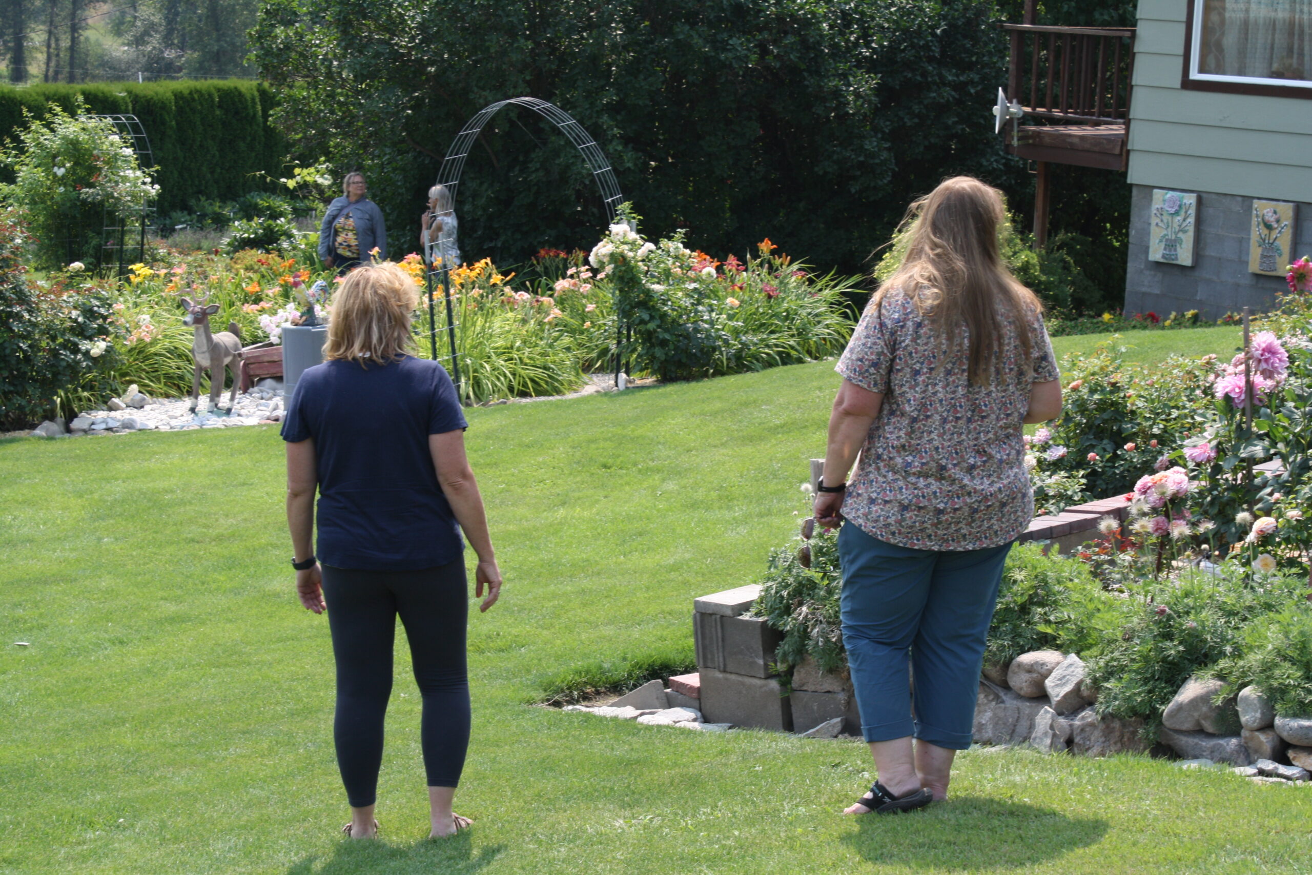 Two women walking through a landscaped garden with flowers and lawn near a house.