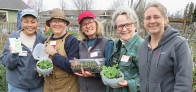 Five Gardeners pose for a picture while holding seed packets and plant starts.