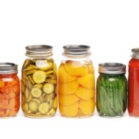 Glass jars filled with assorted preserved vegetables lined up in a row.