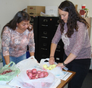 Two people around a table looking at potatoes and onions.