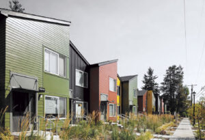 Row of modern, colorful townhouses with tall grass landscaping along a quiet sidewalk.