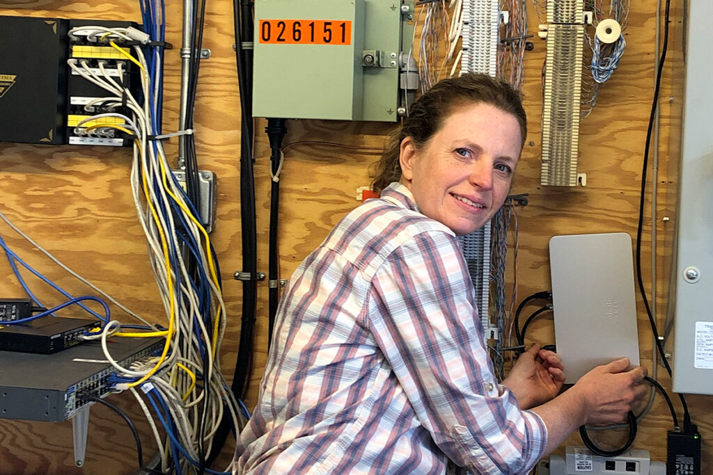 Person in a plaid shirt working with network cables and electrical equipment mounted on a wooden wall.