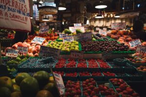 Colorful fruit stand at a market displaying a variety of berries, apples, and other fresh produce with handwritten price signs.