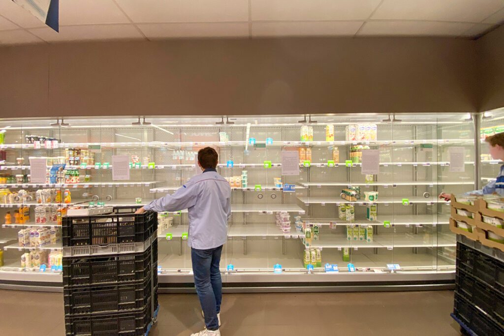 Two people restocking nearly empty refrigerated shelves in a grocery store dairy section.