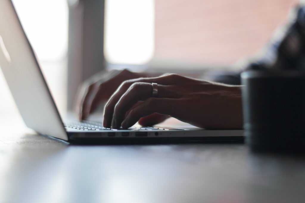 Close-up of hands typing on a laptop keyboard, with natural light from a nearby window.