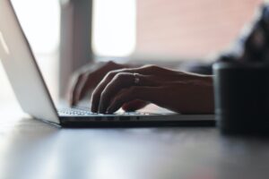 Close-up of hands typing on a laptop keyboard, with natural light from a nearby window.