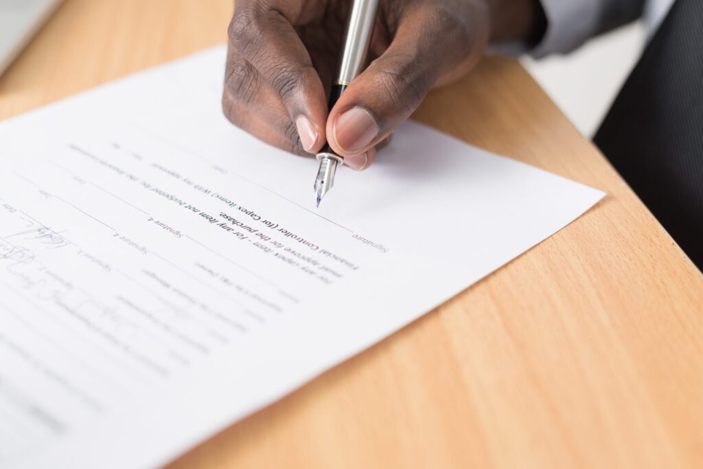 Close-up of a person signing a document with a pen at a wooden desk.