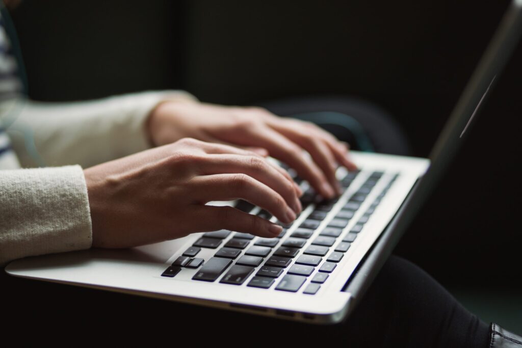 Close-up of a person’s hands typing on a laptop keyboard in a dimly lit setting.
