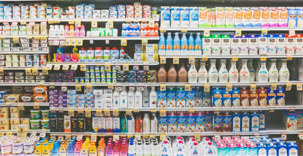 Fully stocked grocery store dairy aisle with rows of milk, creamers, and other refrigerated products.
