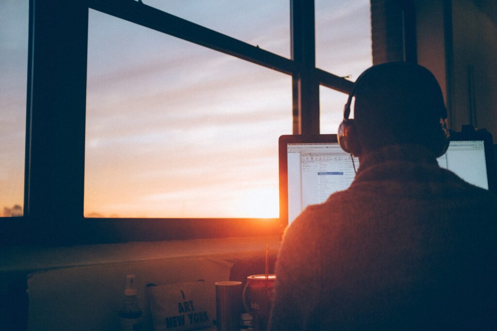 Person wearing headphones working at a computer near a window with a sunset view.