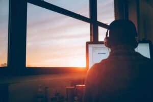 Person wearing headphones working at a computer near a window with a sunset view.