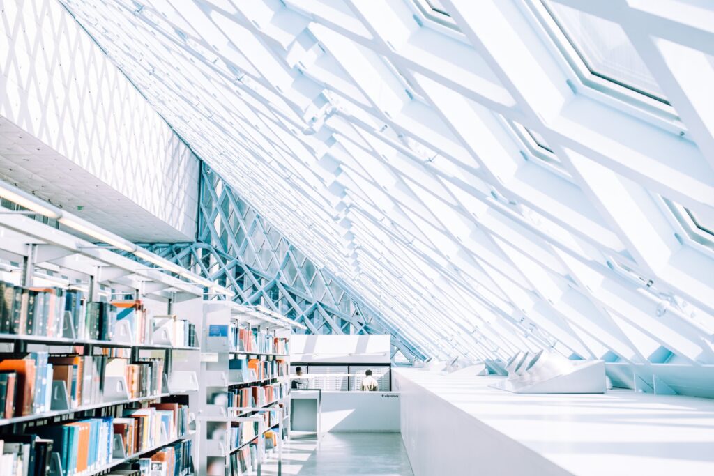 Modern library interior with bookshelves and a geometric glass ceiling allowing bright natural light.
