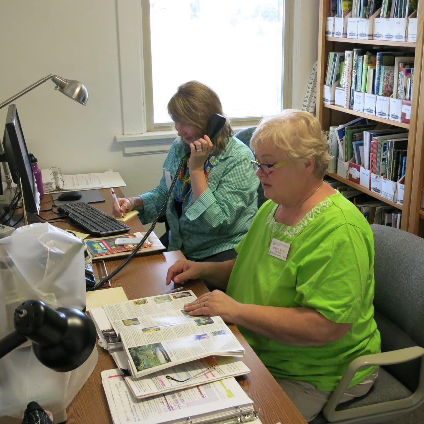 Two Master Gardeners assisting with plant questions at an indoor answer clinic, reviewing materials at a desk