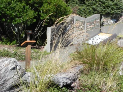 Garden area with tall grasses, rocks, and a small sign, bordered by a decorative fence.