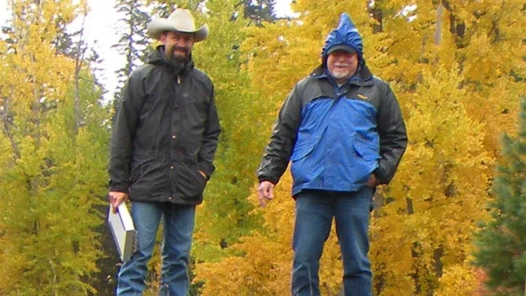 Two people examining exposed soil in a forested area during fall.