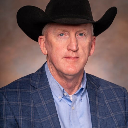 Man wearing a black cowboy hat and blue blazer looks at the camera against a neutral background.