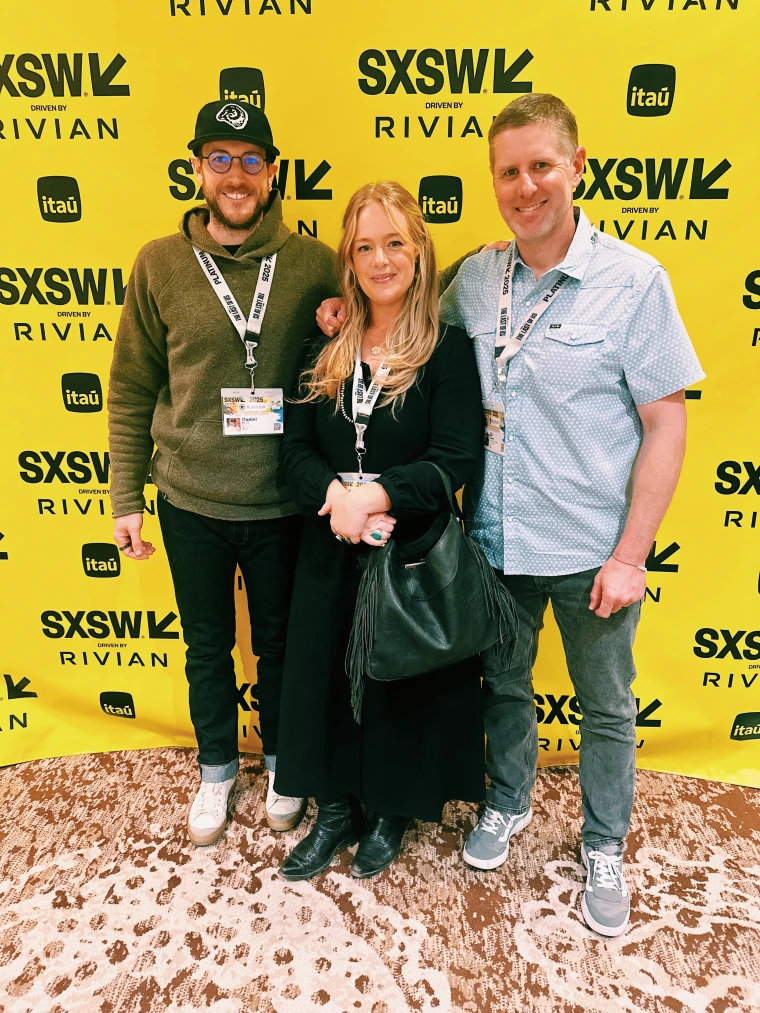 Three people standing together in front of a yellow backdrop.