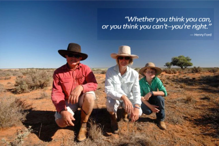 Three people kneeling on the ground with blue sky behind them. 