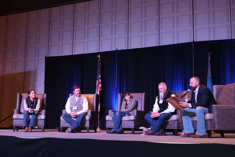 Group of five people sitting in chairs on a stage for a panel discussion.