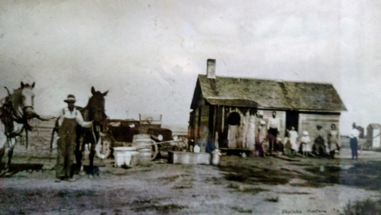 Aged photo of family standing in front of a small home.