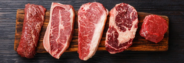 Multiple types and cuts of raw steak on a cutting board. 