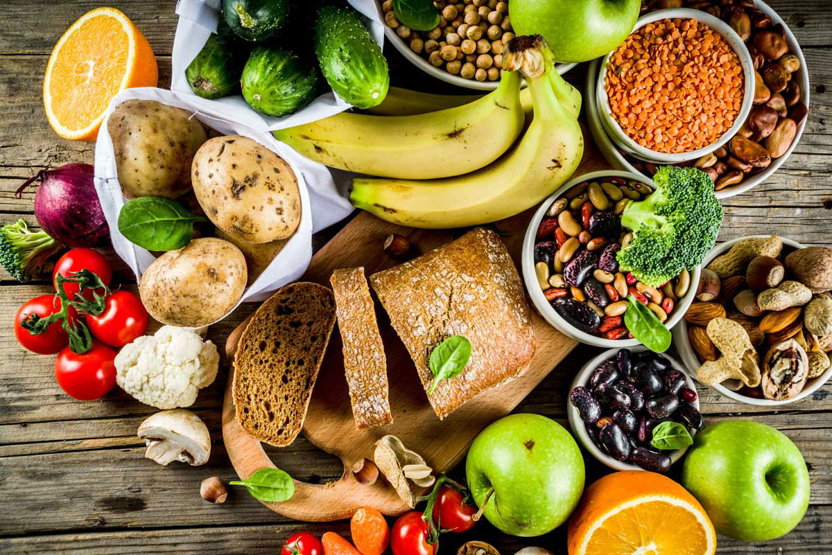 Table full of colorful fruits, vegetables, beans, seeds, and bread.