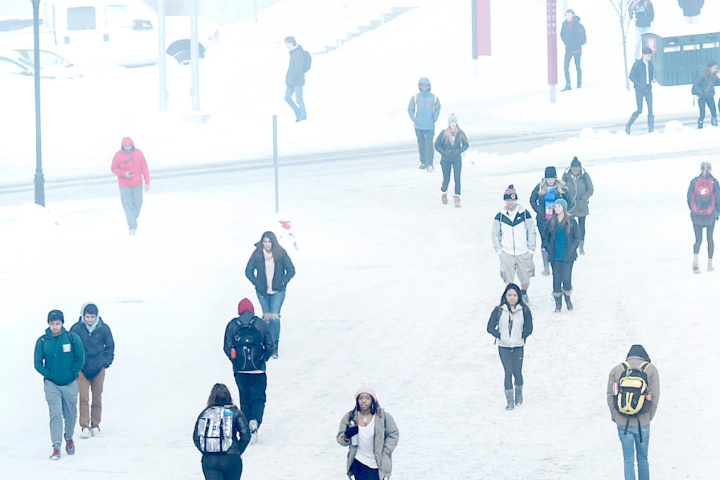 Students in winter weather gear walking through a snowy scene.