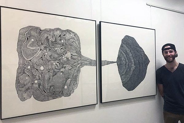 Student stands next to his abstract art piece which is two canvas panels hanging on a blank wall.