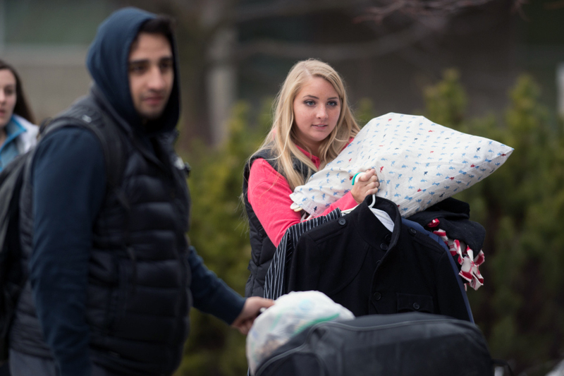 Student holding a pillow while another student is holding a suitcase.