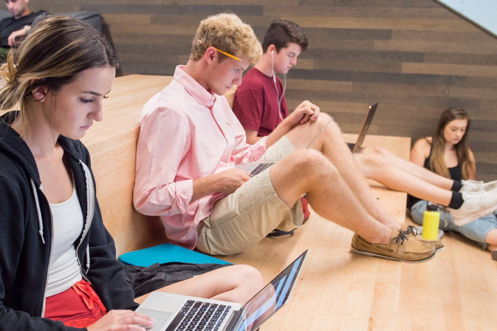 Students sit on a computer on a stair bench
