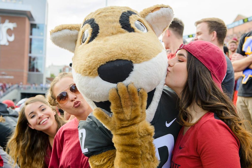 Butch blowing kisses surrounded by female students at football game.