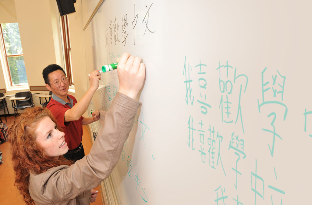A man and woman practicing Japanese handwriting on a white board
