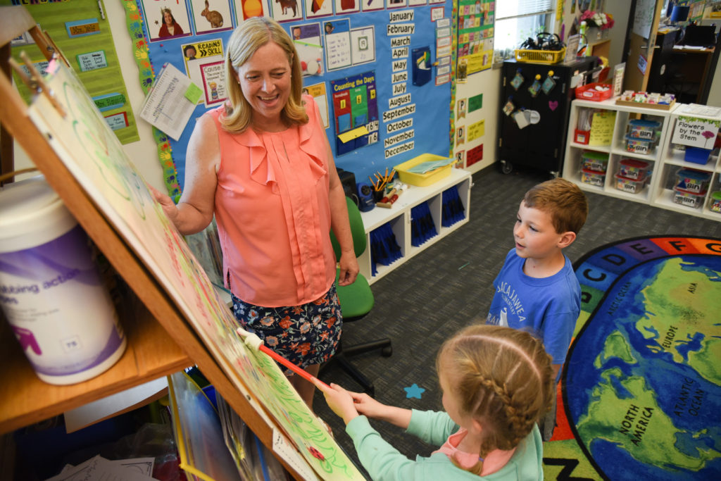 Rausch stands alongside an easel as she works with two kindergarten students.