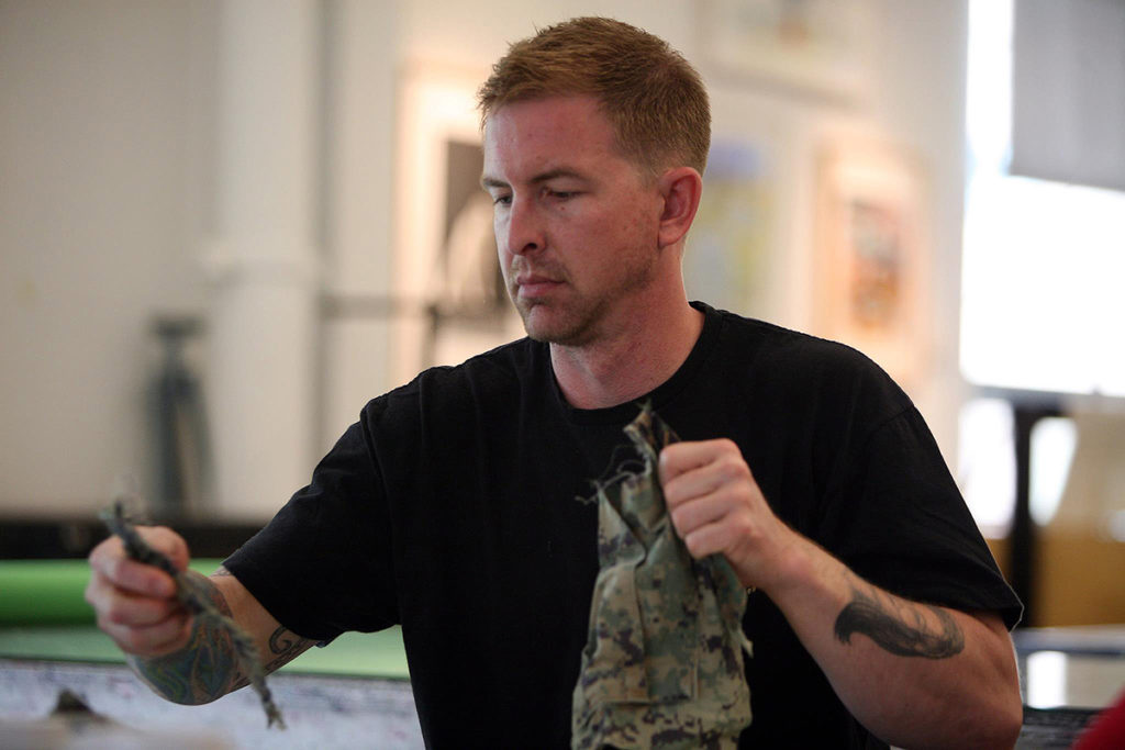 Military veteran tearing uniform material into smaller pieces.