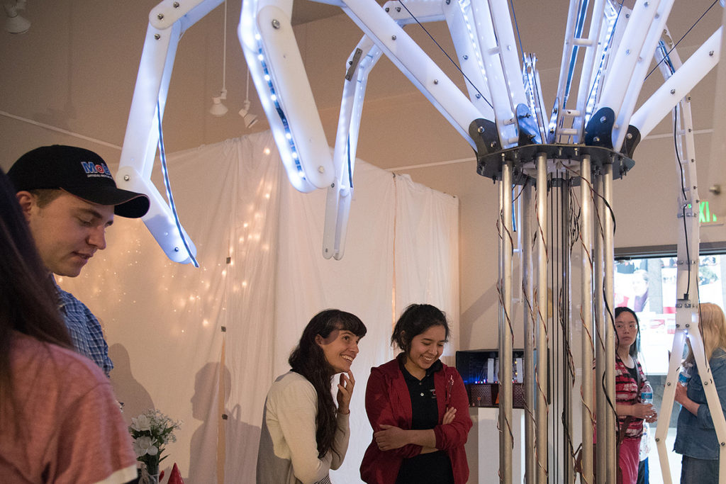 Visitors look at an unusual-shaped robotic structure with lights.