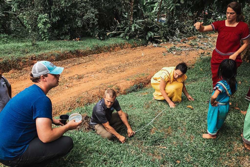People in grassy area use a tape measure and collect water.