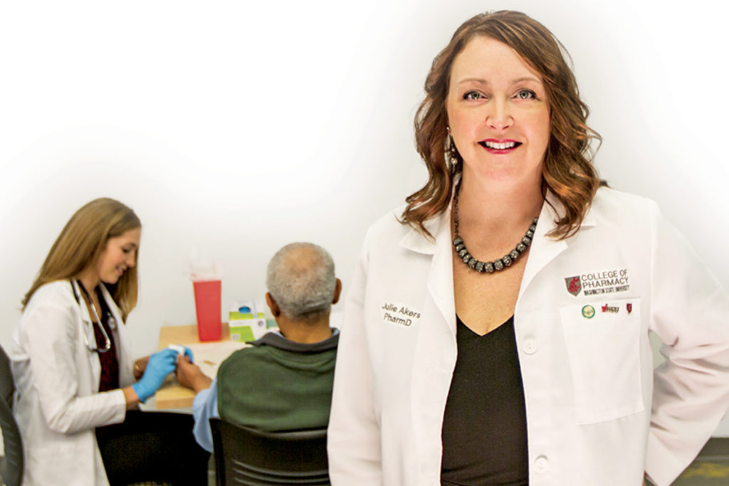 Julie Akers stands in foreground as pharmacy student assists a patient.