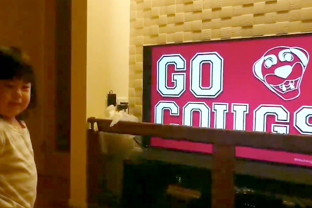 Young girl standing beside TV that says 'Go Cougs'.