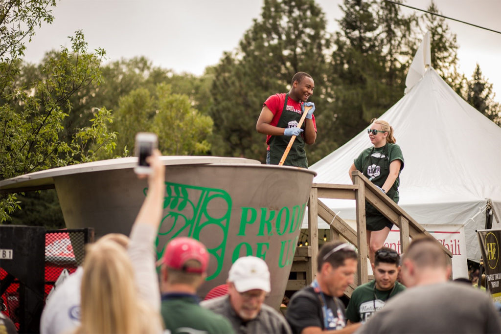 A photograph of the world's largest bowl of lentil chili being stirred by a man with a long wooden spoon at a festival.