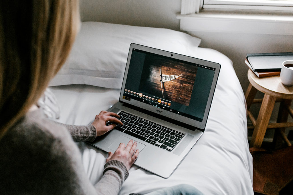 A young woman sitting on her bed using a laptop computer.