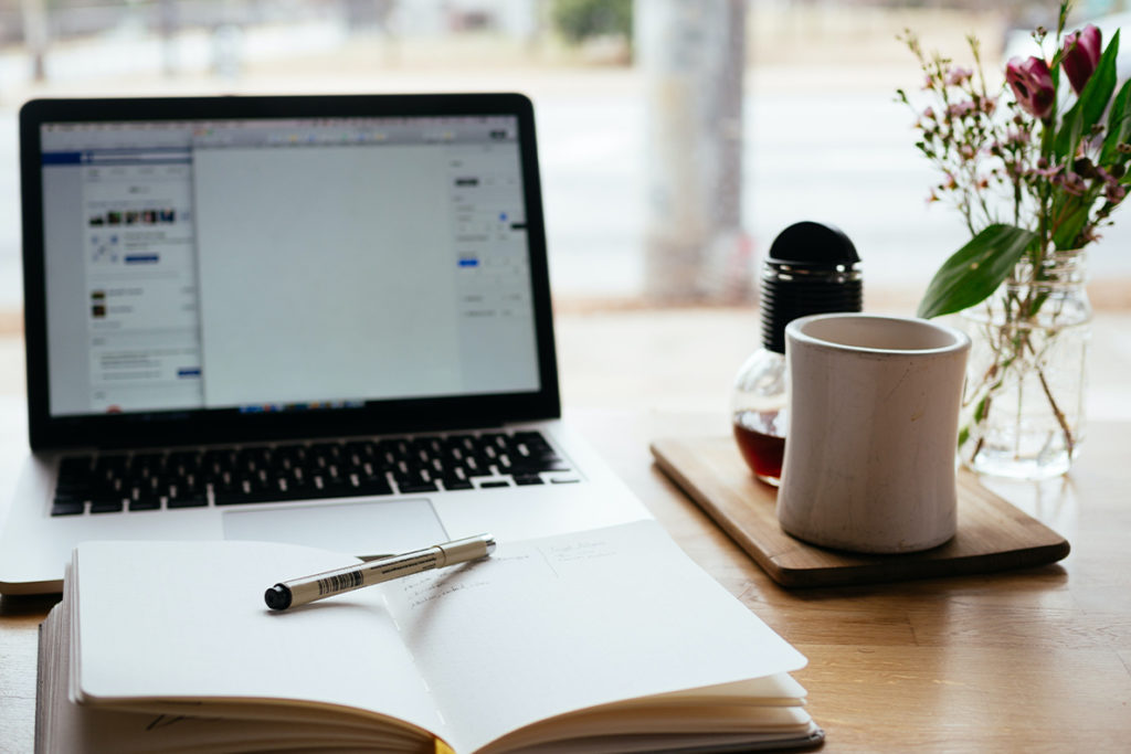 A laptop and book are on a desk in front of a window.