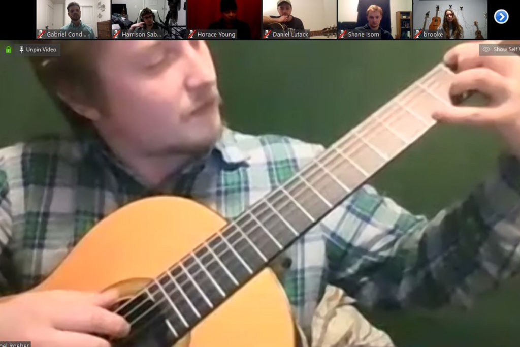 A man plays a guitar while people watch on Zoom.