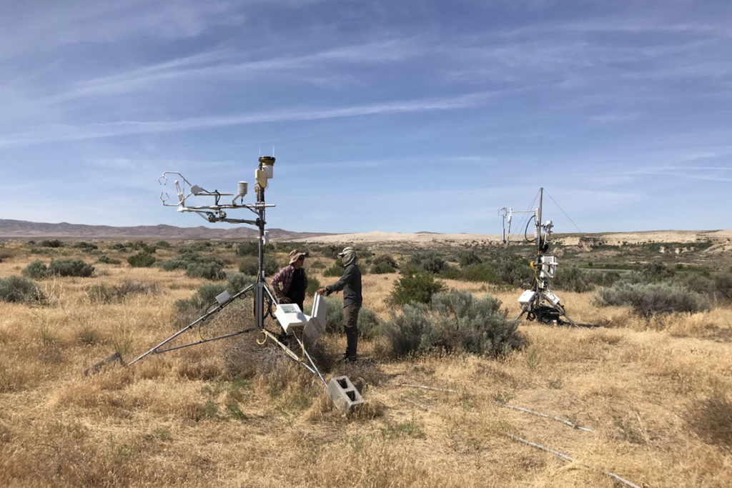 Two researchers standing by measuring equipment on an open stretch of scrubland