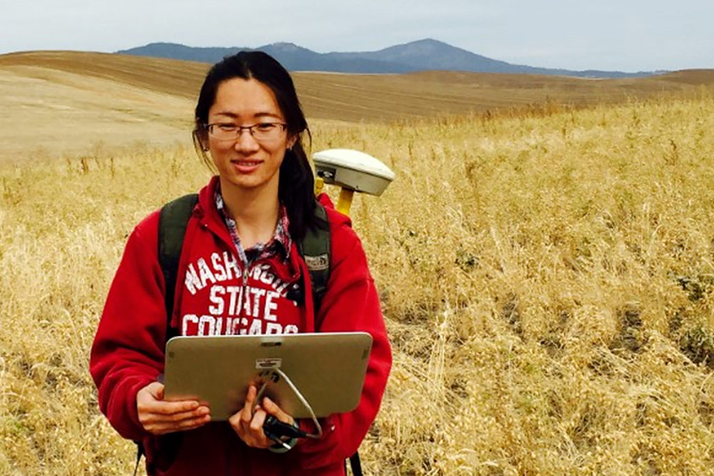 Closeup of Qiuping Peng standing in a field with a computer.