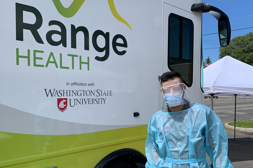 A health care worker in PPE stands next to the WSU mobile health care unit.