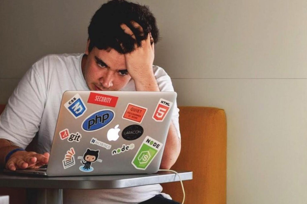 Young man looking stressed as he stares at a computer screen.