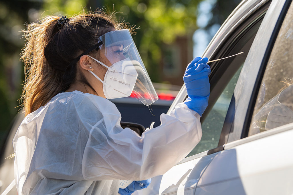 A health care worker reaches through a car window to conduct a COVID-19 test.