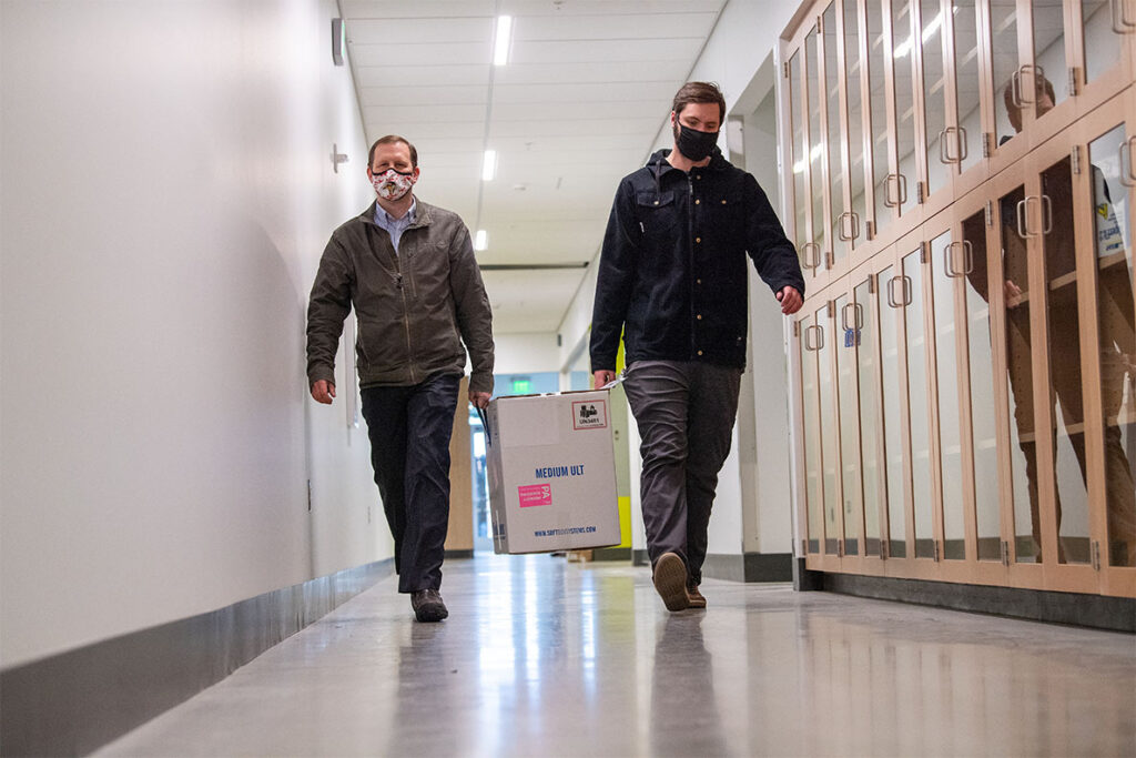 Two people carrying a carton of COVID-19 vaccine down a hallway