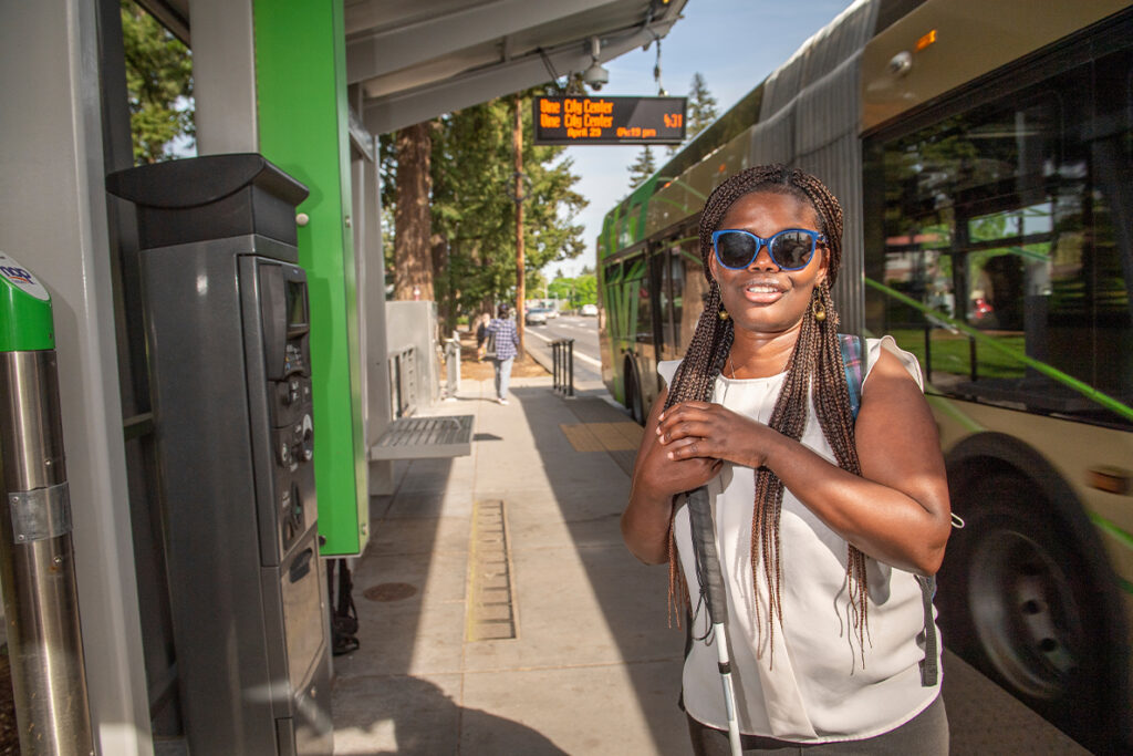 Abby Griffith standing at a bus stop with a bus in the background.